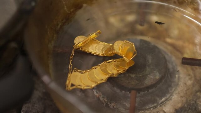 Gold jewelry pieces being cleaned in a chemical bath using tweezers. Shows post-soldering process, oxidation removal and traditional jewelry workshop techniques in a professional setting.

