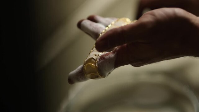 Gold jewelry being cleaned by hand using a brush and soap foam. Shows manual cleaning process, surface preparation and traditional jewelry workshop techniques before polishing.
