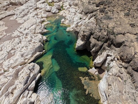Aerial view of turquoise waters wind through the rugged, sun-drenched rocks of Kalysan Canyon, a stark contrast of textures and tones, Kalysan canyon, Socotra, Yemen.