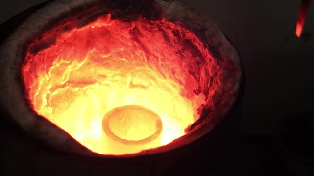 Goldsmith melting gold pieces inside a high-temperature furnace using a crucible. Shows goldsmithing process, metal melting stage and traditional jewelry production in workshop environment.