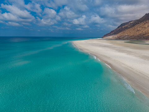 Aerial view of turquoise waters meeting pristine white sands under a sky scattered with clouds near Detwah lagoon, Detwah lagoon, Socotra, Yemen.