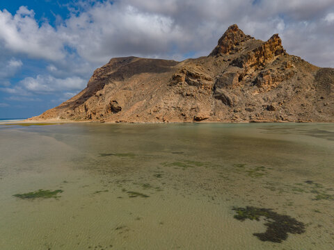 Aerial view of the stark, rocky mountain rising majestically from the tranquil, shallow waters of the lagoon, its slopes meeting the clear, patterned sea, Detwah lagoon, Socotra, Yemen.