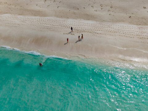 Aerial view of turquoise waters meeting the pristine sands where people gather near 'Socotra' written in the sand, Shoab beach, Socotra, Yemen.