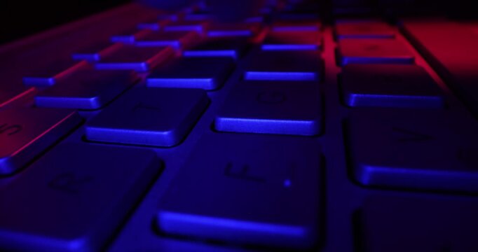close up of fingers typing on computer keyboard in dark room by neon lights. cyber security concept
