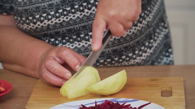 Cutting peeled potato into slices for cooking Ukrainian borscht. Chopping starchy vegetable for preparing traditional soup. Slicing fresh potato pieces for making borscht recipe. Preparing potato