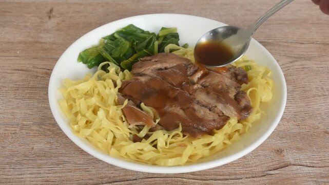 Chinese yellow egg nodles topping braised slice pork leg stew dressing black herb soup couple pickled cabbage and kale dipping spicy sour chili sauce on plate