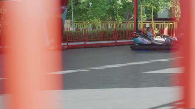 Bumper car ride park weekend closeup view of single bumper car weaving past red safety bars, sunlight dappled trees and wooden fence in background, playful motion blur and summer atmosphere, parent