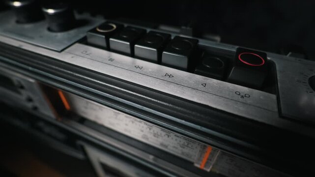 Person finger presses the play button on a vintage silver cassette deck. A close-up view reveals the analog radio dial and retro push buttons. Nostalgic audio technology.