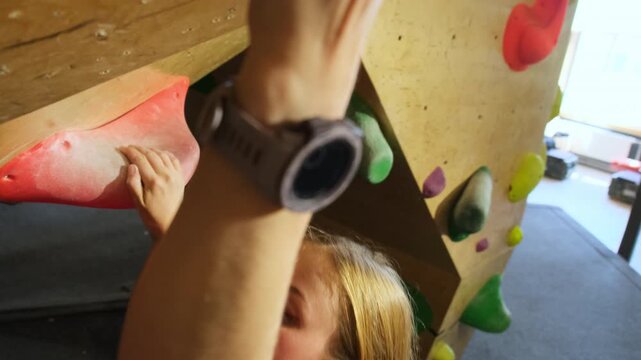 Woman heads up wall grasping hooks tenaciously. Powerful athlete deftly navigates course by deftly grasping ledges on wall