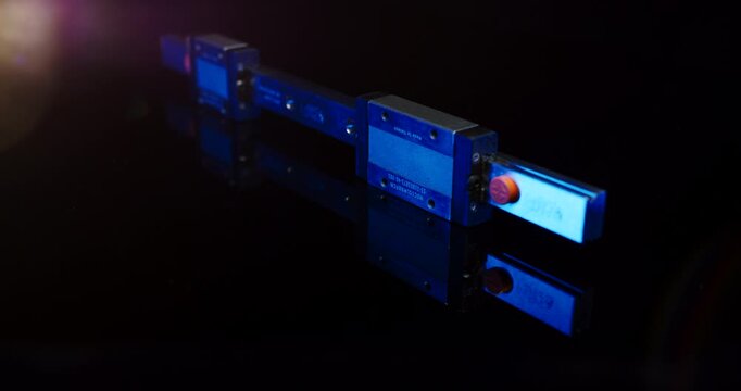 Industrial linear guide rail with two carriage blocks illuminated by blue light in a dark studio