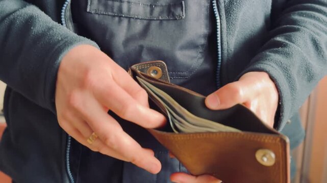 Close up of man hands taking out several hundred dollar bills from brown leather wallet