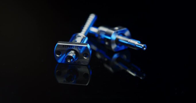 Two precision metallic ball screw spindles with blue light reflection in a dark industrial studio