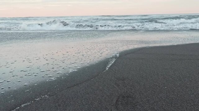 Waves ebb and flow on the Pacific Ocean shoreline, swept by volcanic ash, during the late sunset on the Kamchatka Peninsula. Peace and tranquility