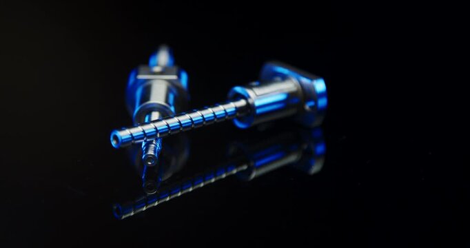 Close up of two metallic precision ball screws with blue lighting on a black reflective surface