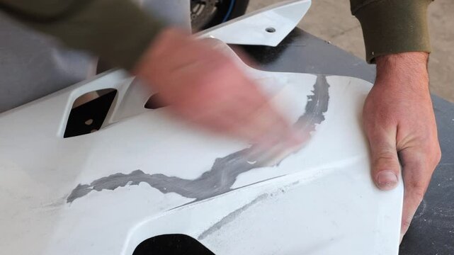 Mechanic amateur sanding motorcycle plastic part before painting in workshop focused on repair and customization