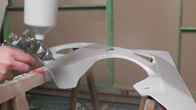 Mechanic amateur painting motorcycle plastic part in small garage focused on repair and customization process