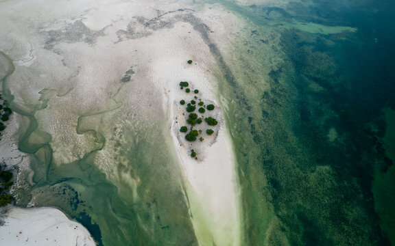 Aerial view of turquoise waters embrace a sandy islet dotted with verdant mangroves, a serene contrast of textures and tones., Paje, Unguja South Region, Tanzania.