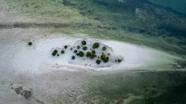 Aerial view of stark white sandbar kissed by shallow turquoise waters, dotted with verdant trees, a tropical jewel revealed from above, Paje, Unguja South Region, Tanzania.