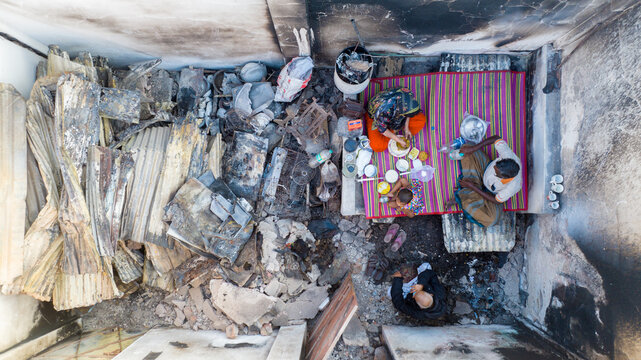 Aerial view of a family sitting on a mat amidst the charred remains of their home, a stark contrast of life and devastation, Dhaka, Dhaka Division, Bangladesh.