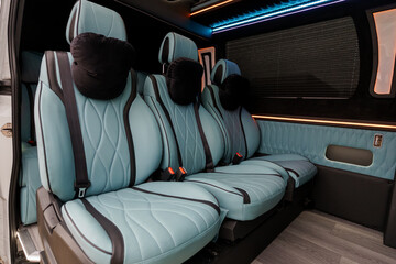 Naklejka premium Interior of a luxury passenger van featuring light blue quilted leather seats and ambient blue LED lighting.
