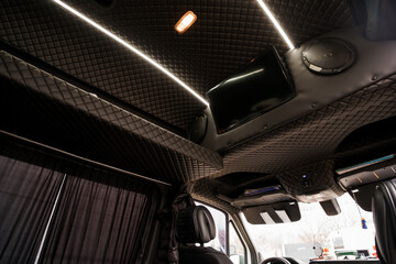 Naklejka premium Luxury Van Interior Featuring Black Quilted Leather Ceiling with Integrated Monitor and Ambient Lighting