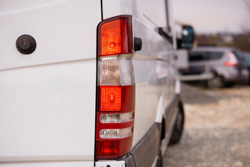 Close up of red and white rear taillight on white commercial delivery van parked outdoors in daylight. © Galka3250