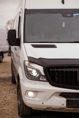 Front view of a white commercial delivery van parked on a dirt road during daylight. © Galka3250