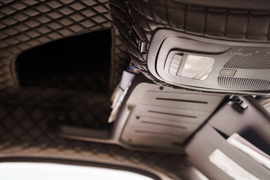 Close up of luxury car headliner with quilted leather texture overhead console light speaker storage compartment black interior detail shot