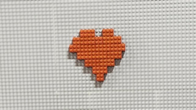 Orange pixel-heart on white pegboard