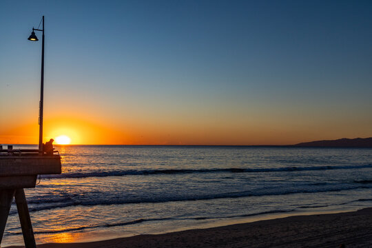 Sun setting above calm ocean and Venice Pier