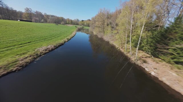 fpv drone flying over forest and pond with cloud relections and algae on a sunny spring day in Vosges region