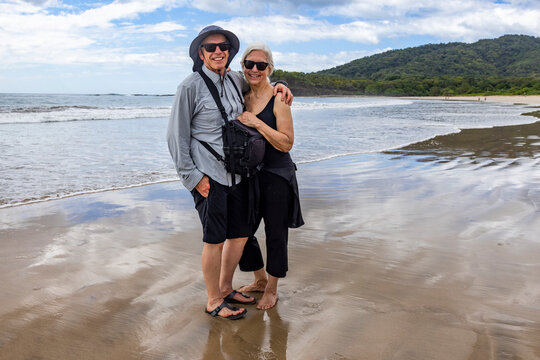 Portrait of smiling senior couple on empty beach at low tide