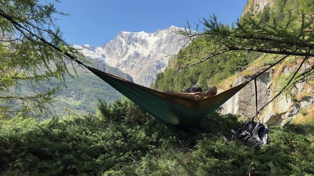 Relaxing in hammock with Monte Rosa glacier view, Macugnaga Italy, summer alpine landscape, hiker resting during trekking, peaceful nature vacation in the mountains