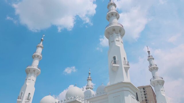 Depok, Indonesia (April 6, 2026): At-Thohir Mosque, A stunning view of mosque minarets reaching into a vibrant blue sky filled with soft clouds, showcasing Islamic architecture in a peaceful urban