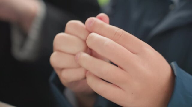 Child uses fingers to mold small eraser outdoors. Children practicing fine motor skills with tiny red object outside. Young child carefully pinches and molds small red eraser on bench