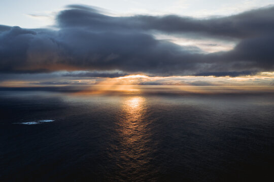 Aerial view of sunbeams piercing through brooding clouds, casting a golden glow on the tranquil waters of the Norwegian Sea, Henningsvaer, Nordland, Norway.