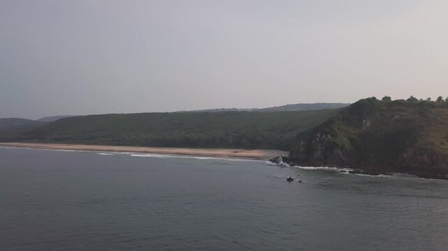 Coastal view of Bhogave Beach in Malvan, Maharashtra showing serene turquoise waters, sandy shoreline, rocky cliff formations, and lush green hills along the Arabian Sea coast