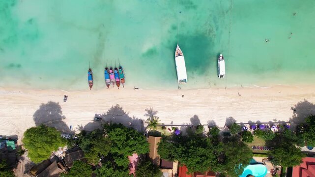 Beautiful drone footage of a beach on Koh Phi Phi in Thailand. Boats are anchored in the turquoise blue water.