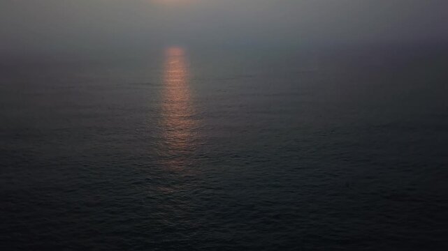 Sunset glowing through hazy atmosphere over the Arabian Sea at Candolim Beach, Goa, India. Golden light reflects on calm dark ocean water creating a luminous pathway during twilight hour.