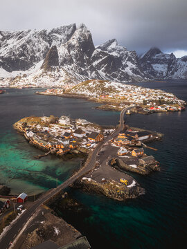 Aerial view of the quaint village nestled on Sakrisoya island connected by bridge, with snow-dusted mountains rising in the background, Sakrisoya, Nordland, Norway.