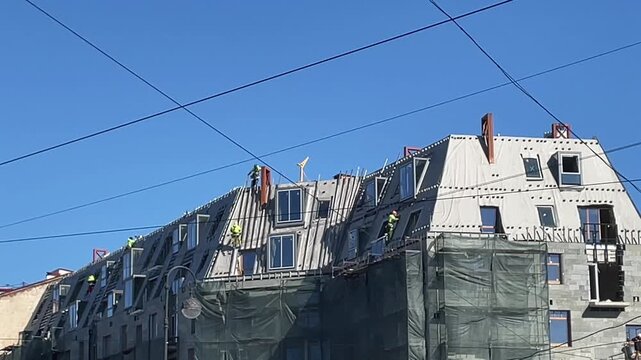 Construction workers on building facade installing panels at height, renovation site with scaffolding and safety gear, modern architecture exterior work under blue sky