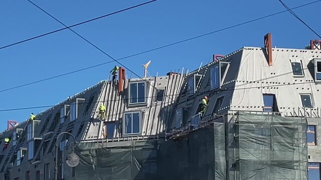 Construction workers on building facade installing panels at height, renovation site with scaffolding and safety gear, modern architecture exterior work under blue sky