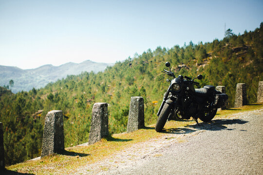 Black motorcycle parked on a mountain road with scenic forested hills and valley in Portugal, travel and freedom concept.