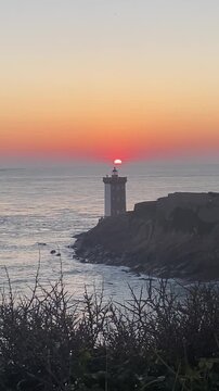 Sunset over Atlantic Ocean with Petit Minou lighthouse on rocky cliff and calm sea horizon