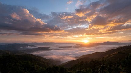 Fototapeta premium Golden sunrise breaks through dramatic clouds above a vast misty expanse of rolling hills
