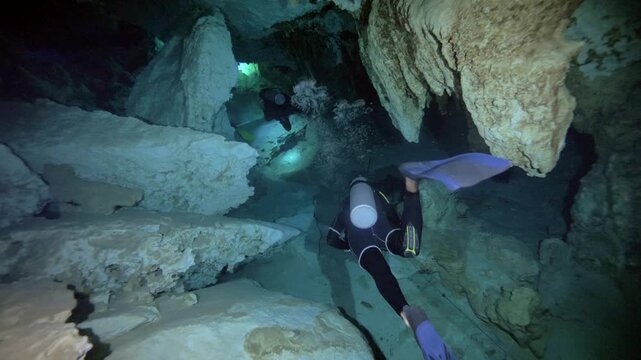 Diver moves through uneven limestone passage with torch light in Cenote Dos Ojos, Quintana Roo, Mexico