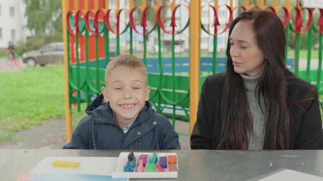 Caucasian boy and teacher prepare back to school with art activity outdoors, shape and color practice, eager grin and marker choice, playful roleplay and supportive guidance for school readiness