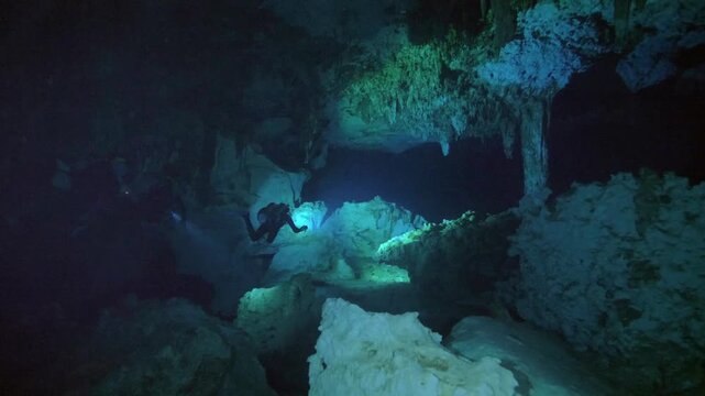 Diver moves through low visibility cavern illuminated by handheld light in Cenote Dos Ojos, Quintana Roo, Mexico
