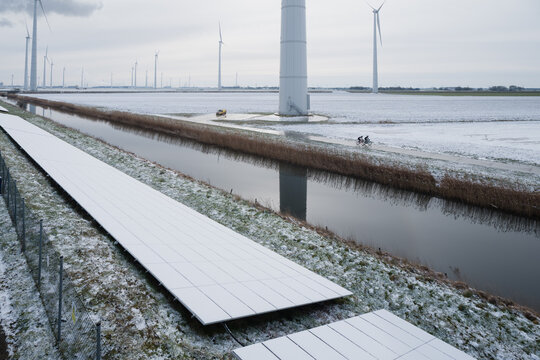 Cyclists Riding Past Wind Turbines and Solar Panels in Winter Landscape &ndash; Renewable Energy Concept