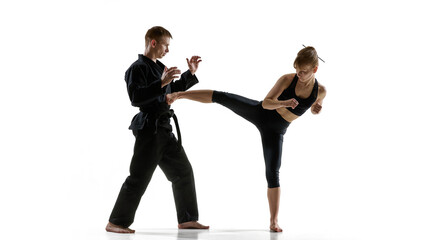 Obraz premium Woman delivering high side kick during martial arts training with partner. Concept of fitness training program, combat sport class, strength conditioning and flexibility improvement.